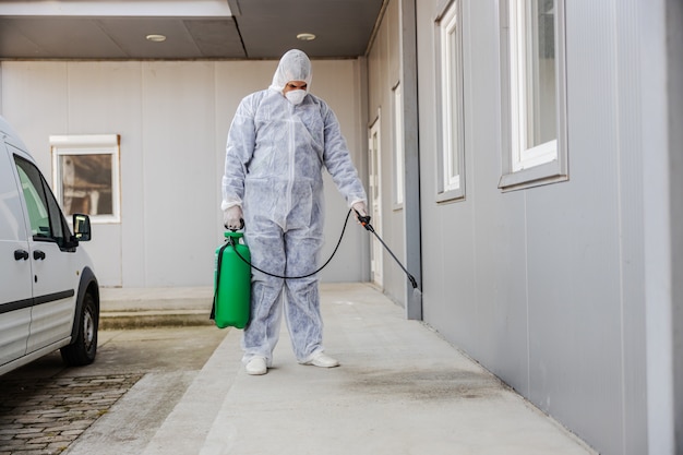 Homme en combinaison de protection contre les virus et masque désinfectant les bâtiments du coronavirus avec le pulvérisateur. Prévention des infections et contrôle de l'épidémie. Pandémie mondiale.