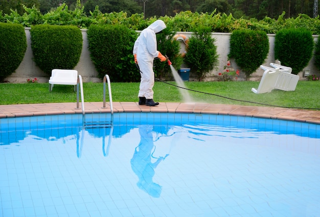 L'homme en combinaison de protection désinfecte le fond de la piscine