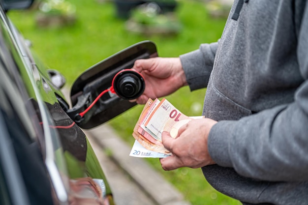 Un homme compte de l'argent debout à un réservoir de carburant ouvert le concept de la hausse des prix du carburant libre