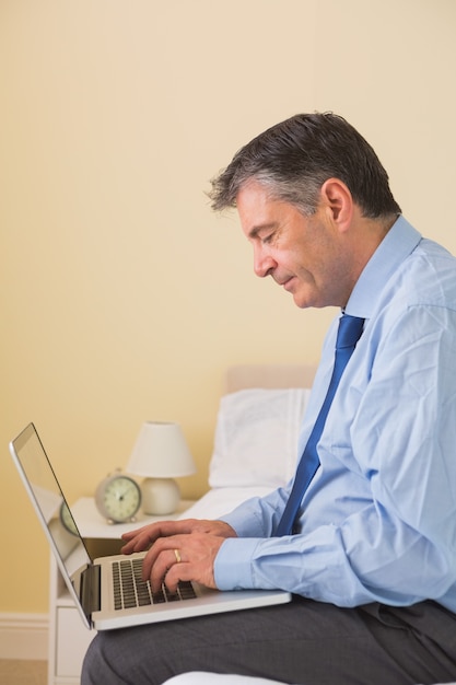 Homme concentré à l&#39;aide d&#39;un ordinateur portable assis sur le lit