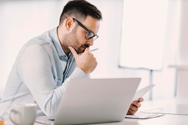 Un homme concentré lisant des documents au bureau à domicile