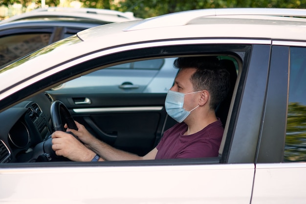 Un homme conduisant une voiture dans un masque médical lors d'une épidémie de coronavirus