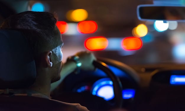 L'homme conduit une voiture dans la ville du soir