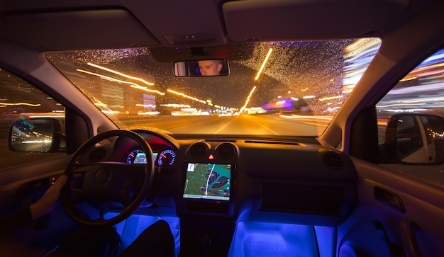 L'homme conduit une voiture dans la ville de nuit. Vue de l'intérieur. Grand angle