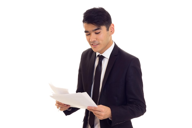 Homme confiant aux cheveux noirs en chemise blanche et costume noir avec une cravate noire tenant des papiers