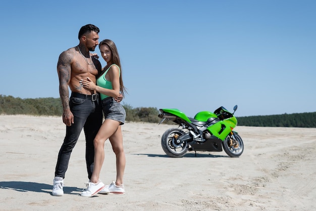 Homme confiant et jeune femme debout et serrant contre la moto dans la campagne