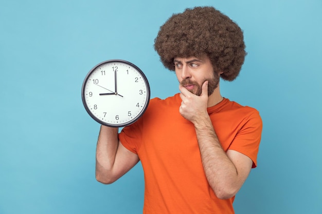 Un homme confus tenant une grande horloge murale et tenant le menton pense à la date limite