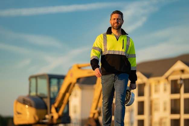 Homme de construction avec excavatrice sur un site industriel ouvrier en casque construit avec un ingénieur bulldozer