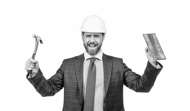 Un homme de construction heureux porte un casque de sécurité avec un costume formel tenant un marteau et une truelle