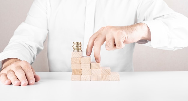 L'homme construit une échelle à partir de blocs de bois avec une pile de pièces au-dessus