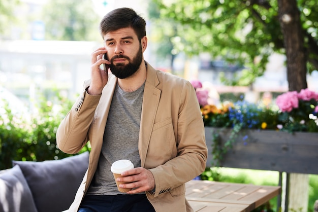 Homme contemporain parlant par téléphone dans un café en plein air