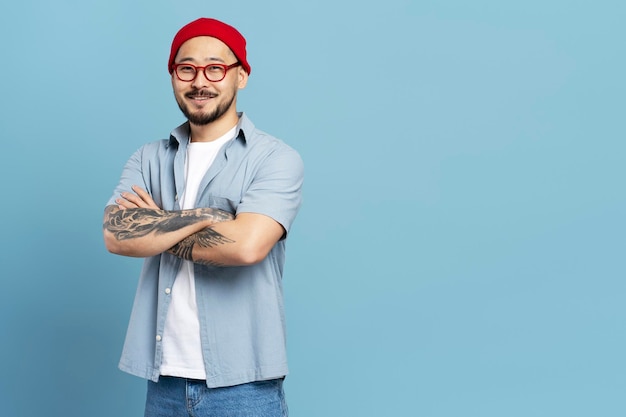 Homme coréen travailleur prospère avec les bras croisés tatouage élégant isolé sur fond bleu