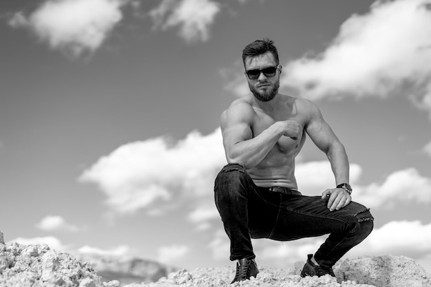 Homme avec un corps parfait pompant des muscles. Assis dans une carrière. Fond de roches grises.