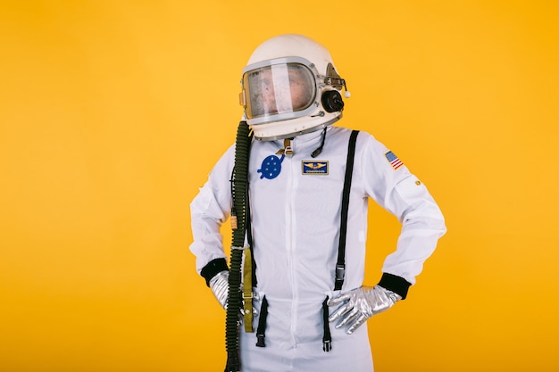 Photo homme cosmonaute en combinaison spatiale et casque avec verre brumeux, bras à la taille, sur le mur jaune.