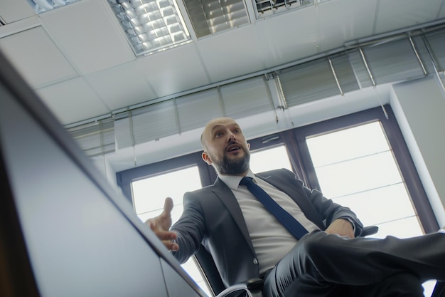 Un homme en costume d'affaires assis sur une chaise dans un bureau en train de parler de quelque chose de bas point de caméra cachée