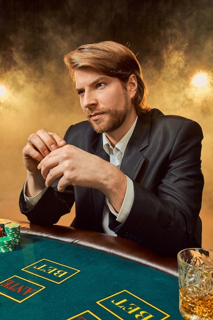 Photo un homme en costume d'affaires assis à la table de jeu. joueur masculin. la passion, les cartes, les jetons, l'alcool, les dés, le jeu, le casino - c'est comme un divertissement masculin.