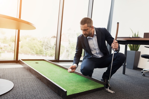 Un homme en costume d'affaires strict joue dans un bureau en mini-golf.