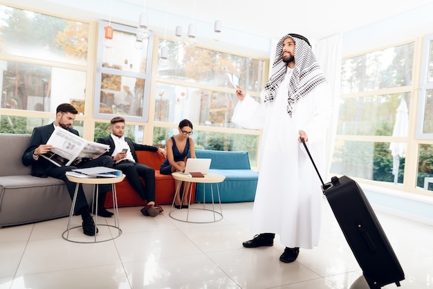 Un homme en costume arabe tient une valise.
