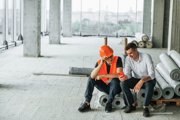 Un homme en costume et un bricoleur en vêtements de protection orange travaillent sur la construction