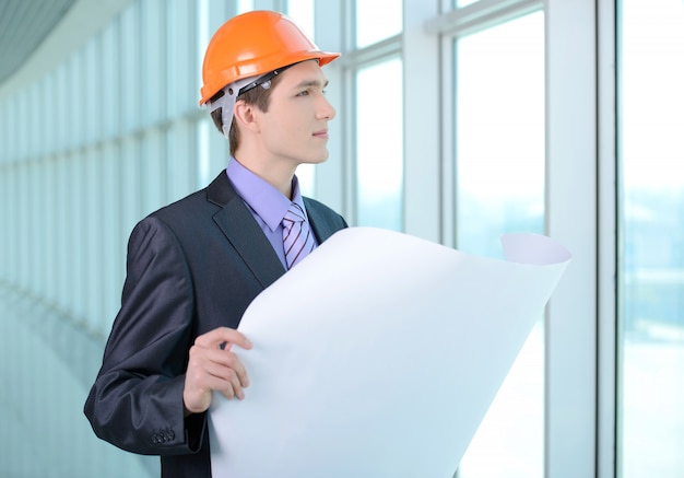 Un homme en costume et casque regarde un plan de construction.