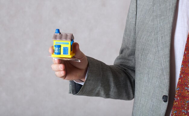 Un homme en costume classique garde une maison en caoutchouc et de l'argent. Closeup.Espace libre pour un texte.