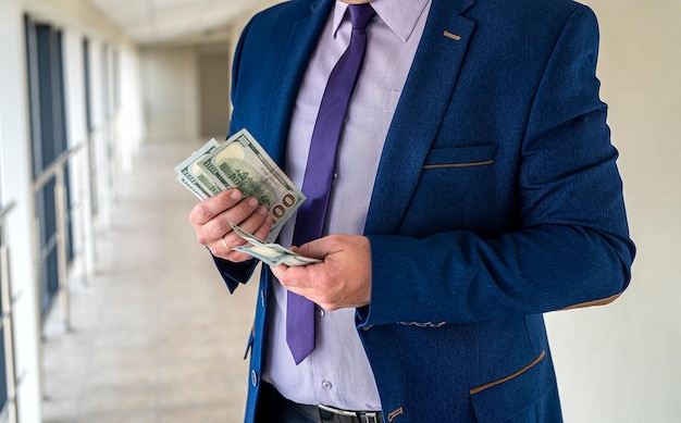 Homme en costume comptant des billets de 100 dollars au bureau. Concept de réussite commerciale