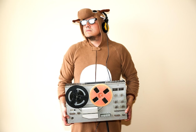 Homme en costume cosplay d'une vache avec magnétophone à bobines. Guy dans les vêtements de nuit pyjama animal. Photo drôle avec des idées de fête. Musique rétro disco.