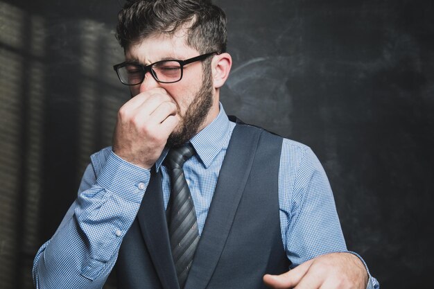 Homme en costume couvrant son nez de dégoût sur fond gris