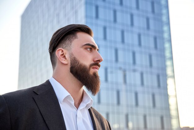 Homme en costume debout devant des gratte-ciel appelant avec lui travailler au bureau. Jeune homme d'affaires caucasien.