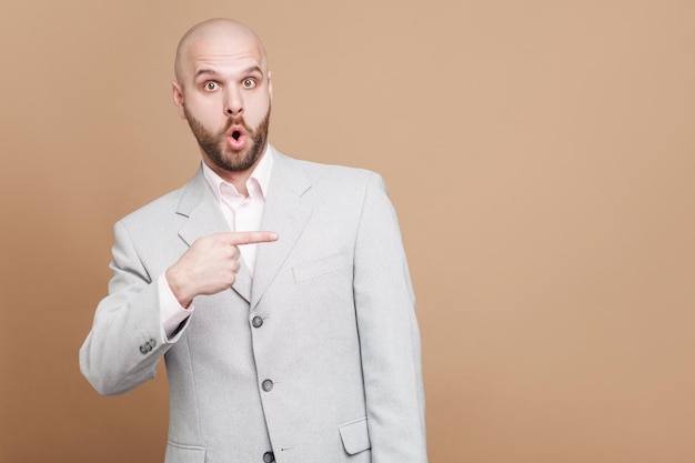 Homme en costume debout regardant la caméra se demandant et montrant un fond marron