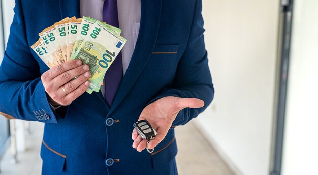 Un homme en costume détient des euros et des clés de voiture. louer ou acheter une voiture. concept de magasinage