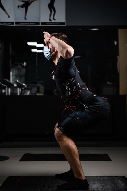 Homme en costume EMS et masque médical dans une salle de sport