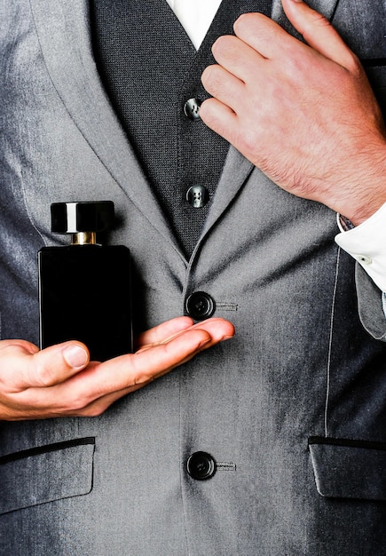 Homme en costume formel, bouteille de parfum, gros plan. Odeur de parfum. Parfums pour hommes. Bouteille d'eau de Cologne tendance. Homme tenant une bouteille de parfum. Parfum d'hommes à la main sur fond de costume.