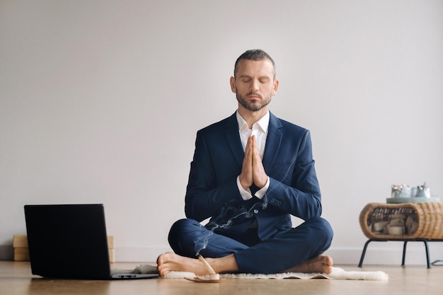 Un homme en costume formel médite assis dans une salle de fitness avec un ordinateur portable