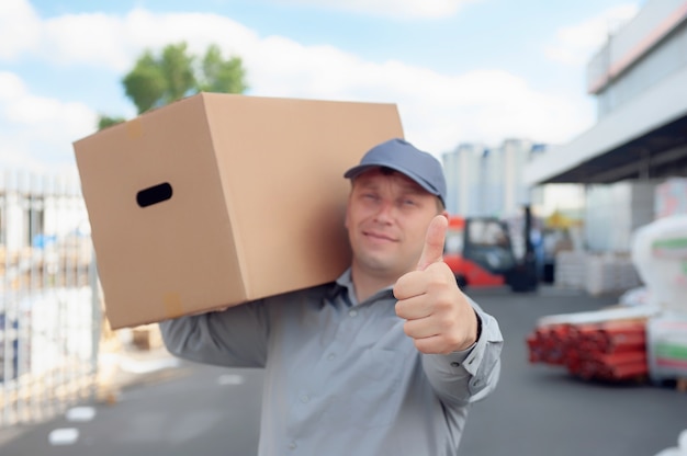 Un homme en costume gris dans ses mains avec une boîte en carton dans le contexte d'un entrepôt et d'un chargeur