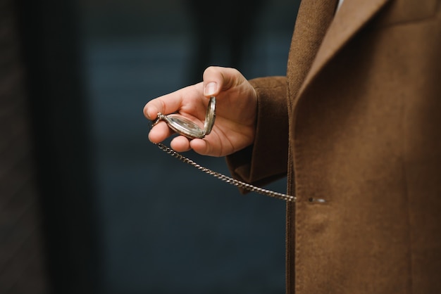 Un homme en costume gris tient une montre de poche dorée.