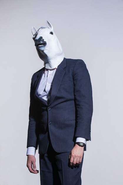 Un homme en costume et un masque de cheval sur fond clair. Contexte conceptuel des affaires