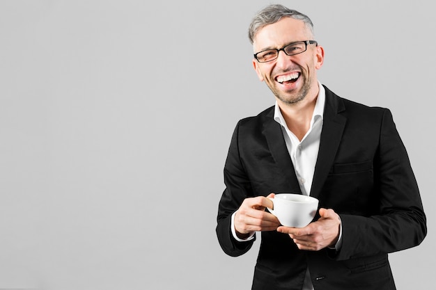 Homme en costume noir tenant une tasse de café et des sourires