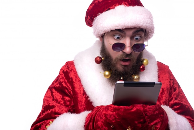 Homme en costume de père Noël, lunettes noires et jouets de Noël dans une barbe tenant une tablette Copy-Space