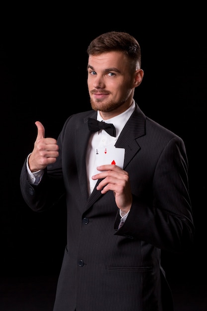 Homme en costume posant avec des cartes pour le jeu sur fond noir