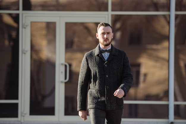 Un homme en costume et pull pose dans la rue.