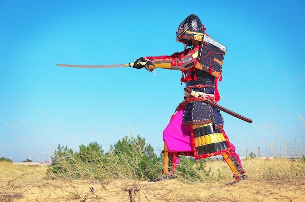 Homme en costume de samouraï avec épée. Samouraï en armure ancienne dans un champ avec épée. Caractère original.