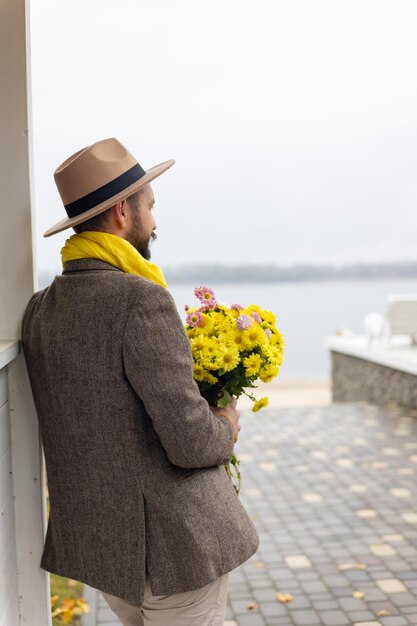 un homme en costume se tient avec des fleurs jaunes au bord de la rivière