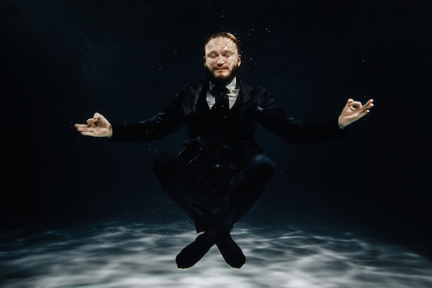 Un homme en costume strict sous l'eau en position Lotus