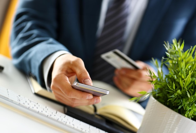 Un homme en costume tient une carte de crédit et un téléphone.