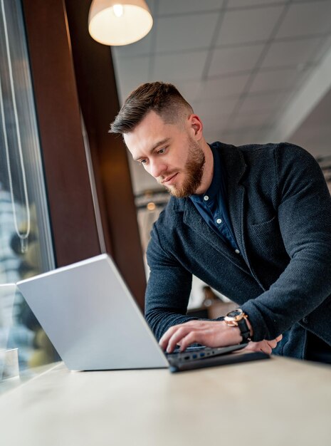 Homme en costume travaillant au restaurant sur ordinateur portable. Portrait d'un jeune homme d'affaires dans un café.