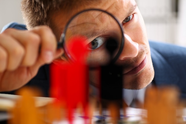 Homme en costume à travers la loupe sur les statuettes gros plan au bureau. Succès évaluation RH personnes inspecteur chasseur de têtes demandeur échange concept