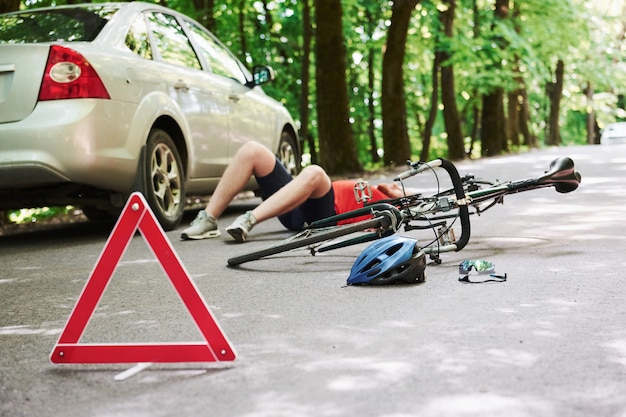 Homme couché. Victime sur l'asphalte. Location et accident de voiture de couleur argentée sur la route en forêt pendant la journée