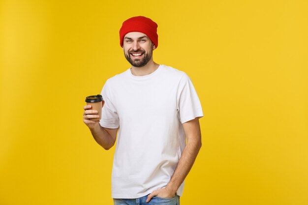 Homme sur une couleur jaune vibrante isolée prenant un café dans une tasse de papier à emporter et souriant car il commencera bien la journée.