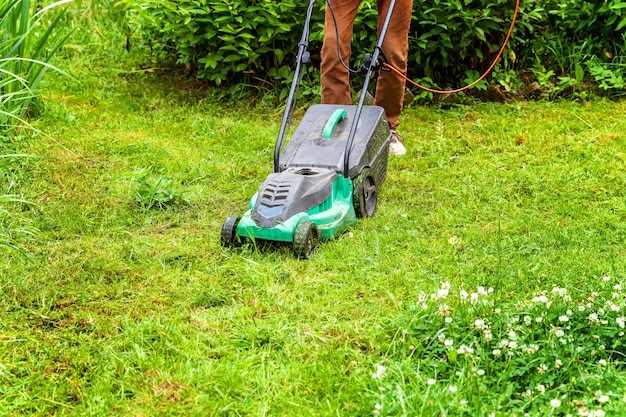 Homme coupant l'herbe verte avec une tondeuse à gazon dans l'arrière-cour Arrière-plan de style de vie pays jardinage Belle vue sur la pelouse d'herbe verte fraîche dans le paysage de jardin de la lumière du soleil au printemps ou en été